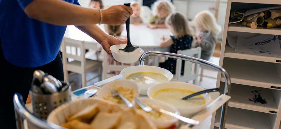En vuxen som plockar mat framför förskolebarn.