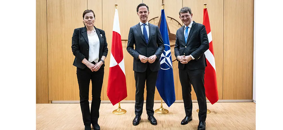 En kvinna och två män framför flaggor.